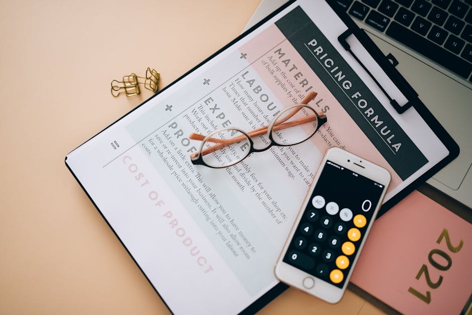 Overhead view of business tools including a phone calculator, pricing formula document, and eyeglasses on a desk.